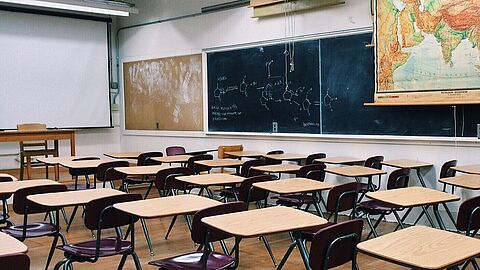 Foto van een klaslokaal met stoelen, bureaus, schoolbord en landkaart