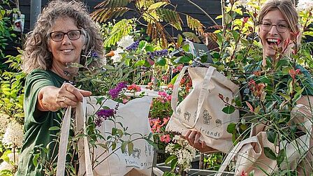 Op de foto: Petra Ekhardt (l) en Corienne Merkens van Merkens Tuincentrum met de gratis planten in canvas tassen